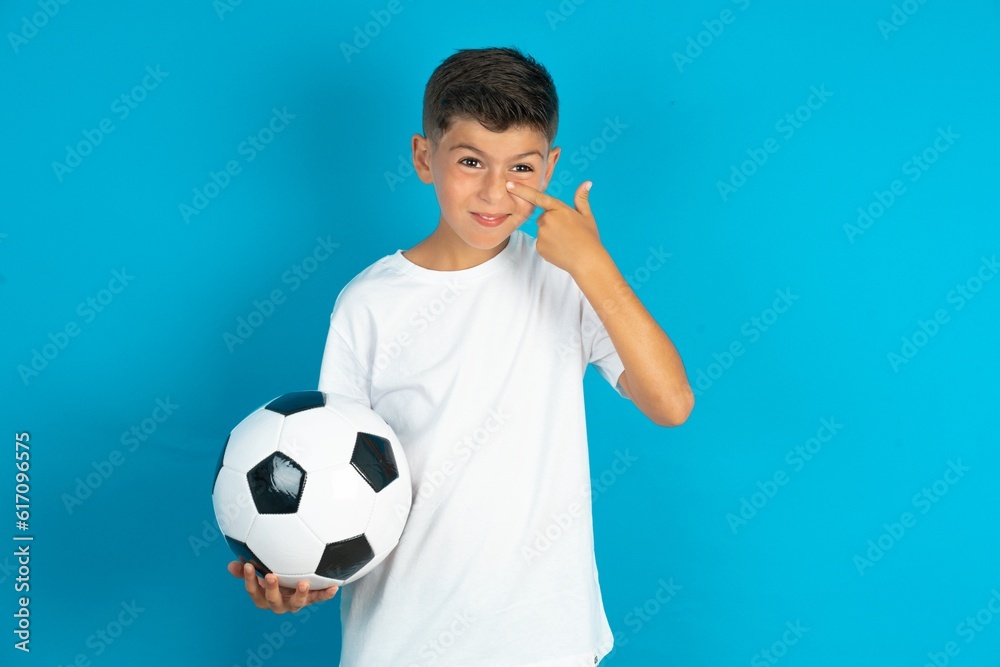 Little hispanic boy wearing white T-shirt holding a soccer ball pointing unhappy to pimple on forehead, ugly infection of blackhead. Acne and skin problem Little hispanic boy wearing white T-shirt holding a soccer ball pointing unhappy to pimple on forehead, ugly infection of blackhead. Acne and skin problem
