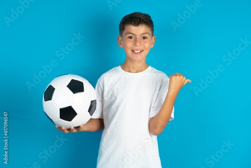 Charming Little hispanic boy wearing white T-shirt holding a soccer ball looking at copy space having advertisements