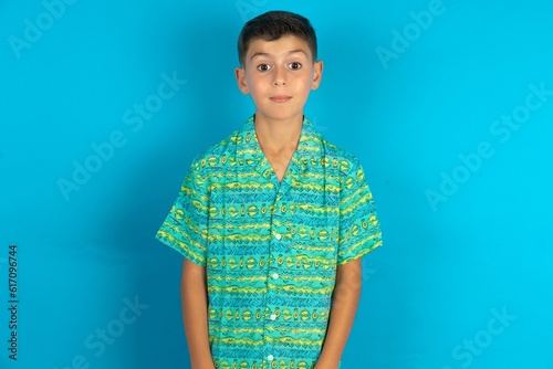 Stunned Little hispanic boy wearing green aztec shirt stares reacts on shocking news. Astonished MODEL holds breath