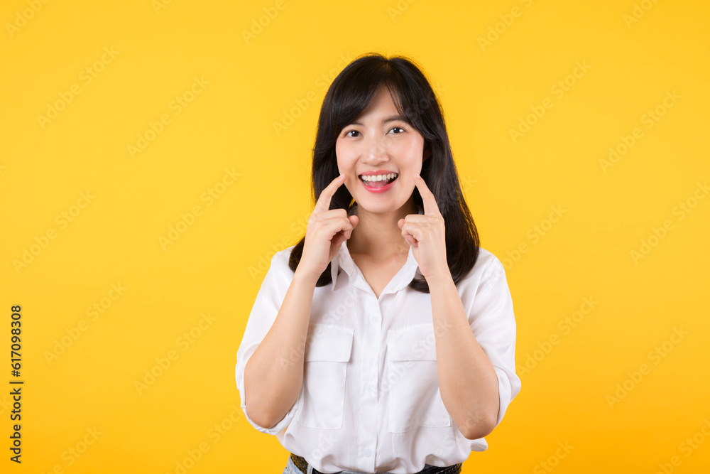 Young beautiful asian woman happy smile wearing white shirt and denim jean plants over yellow isolated background smiling confident showing and pointing with fingers teeth and mouth. Dental concept. Young beautiful asian woman happy smile wearing white shirt and denim jean plants over yellow isolated background smiling confident showing and pointing with fingers teeth and mouth. Dental concept.