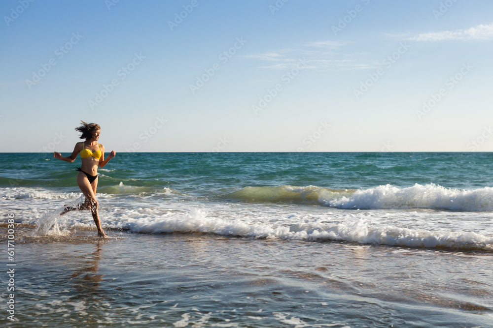 A woman in a bathing suit rests on the sandy seashore and bathes in the waves