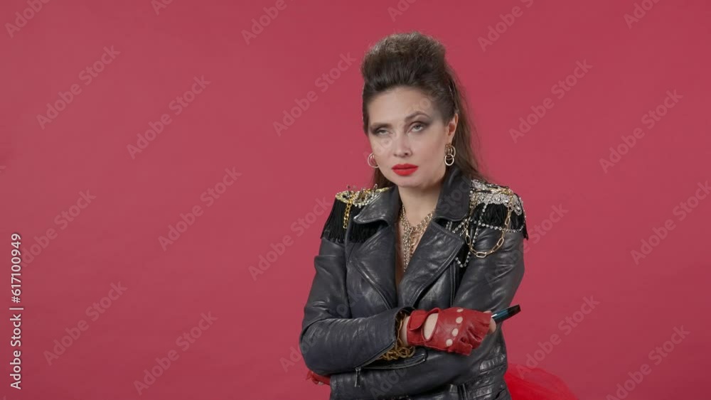 A woman smokes an electronic cigarette and blows smoke from her mouth in a circle. Portrait of freak woman with crossed arms on sternum over red background in studio. HDR BT2020 HLG Material. A woman smokes an electronic cigarette and blows smoke from her mouth in a circle. Portrait of freak woman with crossed arms on sternum over red background in studio. HDR BT2020 HLG Material.