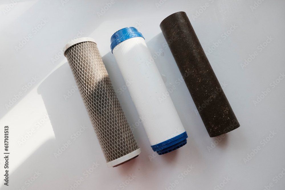 Naklejka premium Electric filter for water purification in the kitchen in the cabinet under the sink. Used dirty filters of varying degrees of purification, three pieces, metal, plastic.