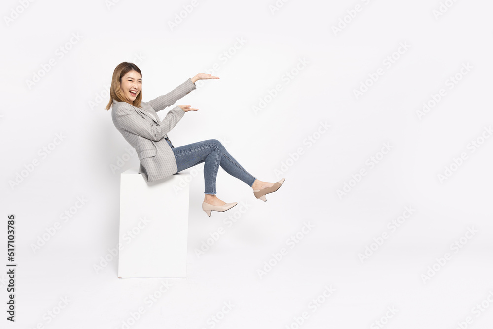 Happy cheerful young Asian businesswoman in suit sitting on white box isolated on white background, Presentation concept Happy cheerful young Asian businesswoman in suit sitting on white box isolated on white background, Presentation concept