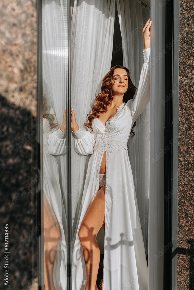 beautiful girl in a white open dress touches poses standing in a white curtain on the balcony window beautiful girl in a white open dress touches poses standing in a white curtain on the balcony window
