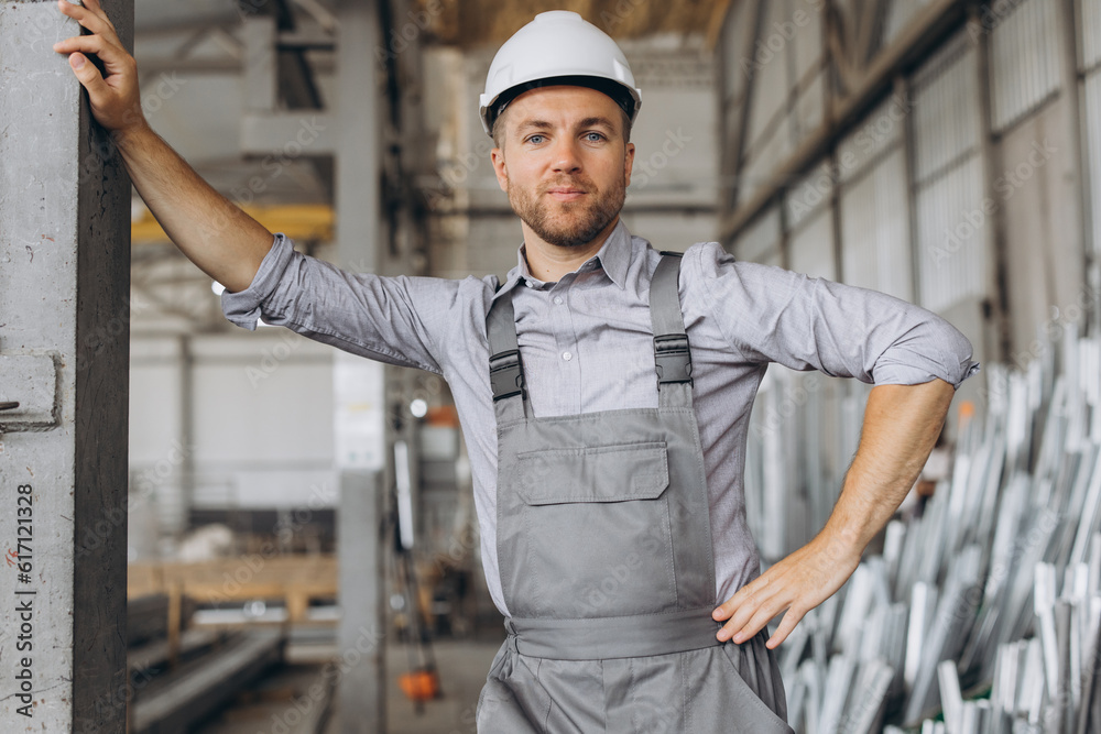 Portrait of a happy worker in a gray uniform and a white hard hat posing on the background of factory production Portrait of a happy worker in a gray uniform and a white hard hat posing on the background of factory production