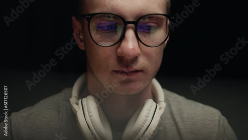 Concentrated young professional programmer in computer glasses with monitors reflection works online late. Serious hacker, IT specialist using laptop computer. Esport player in virtual competition.