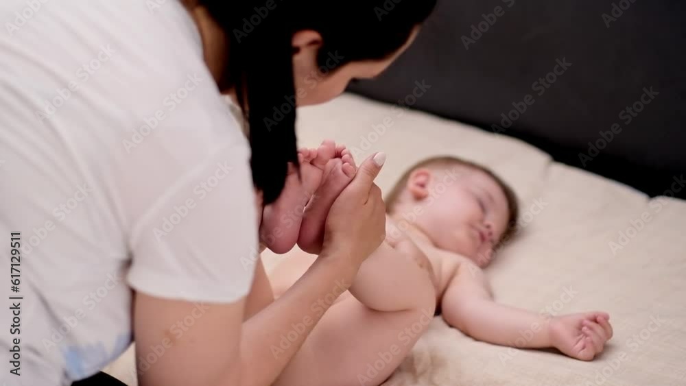 Loving mother holding tiny soft feet of sleepy little son with hands cute barefoot baby sleeping on soft bed at home woman enjoying time with infant in morning closeup Loving mother holding tiny soft feet of sleepy little son with hands cute barefoot baby sleeping on soft bed at home woman enjoying time with infant in morning closeup