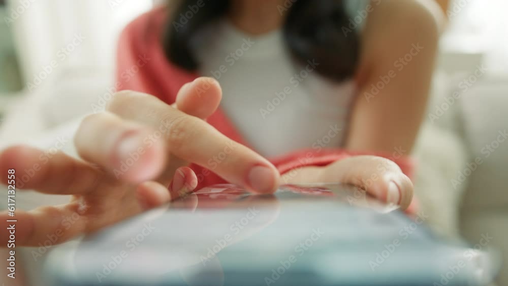 Unrecognizable woman in orange coral sweater sitting on sofa and using smartphone in modern room. Close up female fingers scrolling social media content on cell phone blogging concept slow motion 4K