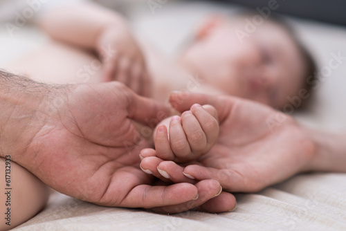 Happy mother and father holding tiny hand of newborn son lying on comfortable bed in morning parents enjoying spending time with little baby at home closeup