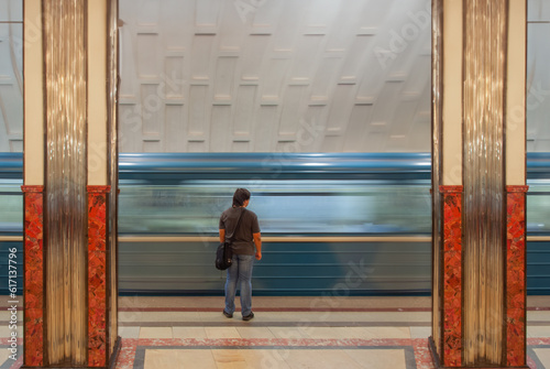 A man standing in a metro station with a passing metro train in the background 