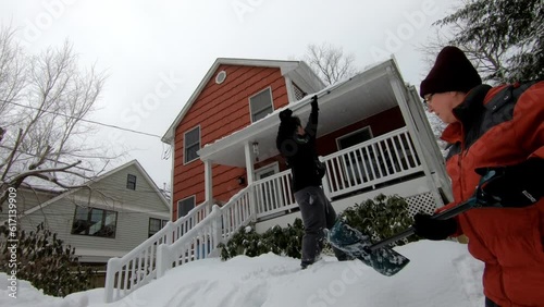 young man removing snow from roof and woman shoveling the snow after the snow storm