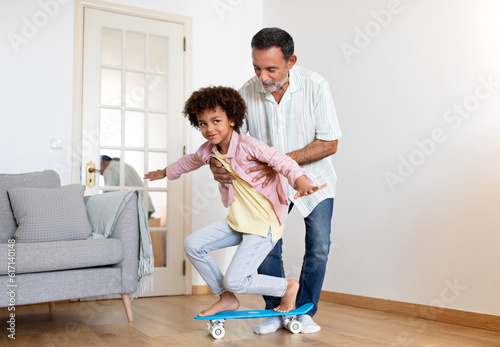 Senior Grandpa Teaching Grandson To Ride A Skateboard At Home © Prostock-studio