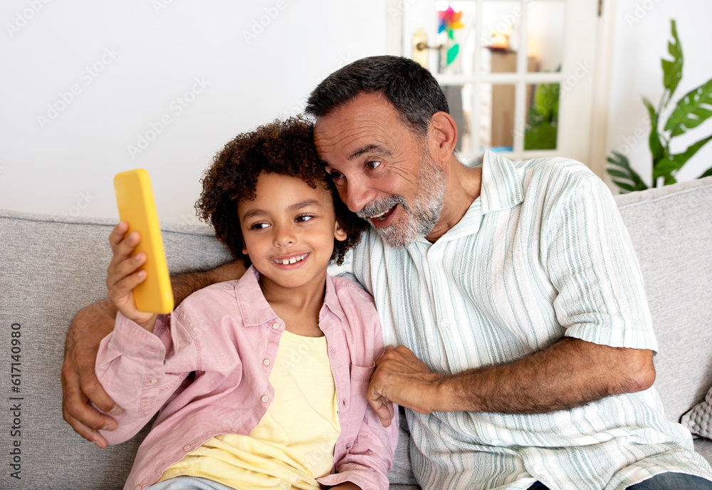 Fototapeta premium Hispanic Grandpa And Grandson Using Cellphone Together At Home
