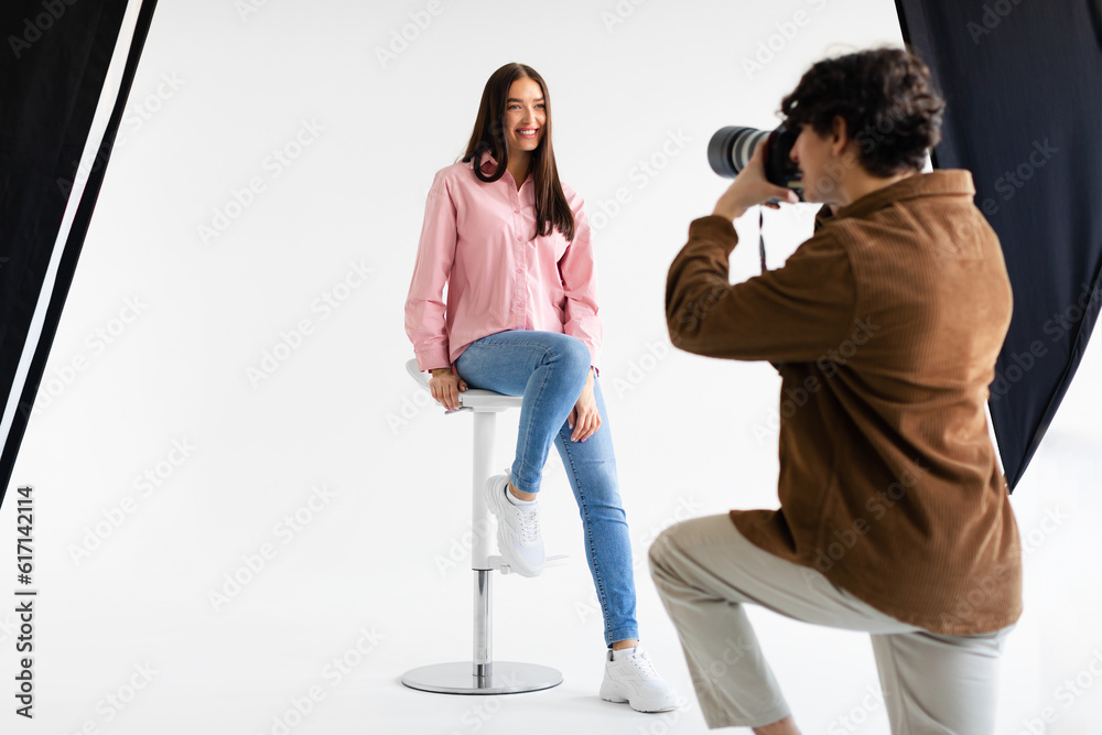 Stylish photoshoot. Male fashion photographer taking picture of young european woman in casual wear - obrazy, fototapety, plakaty 