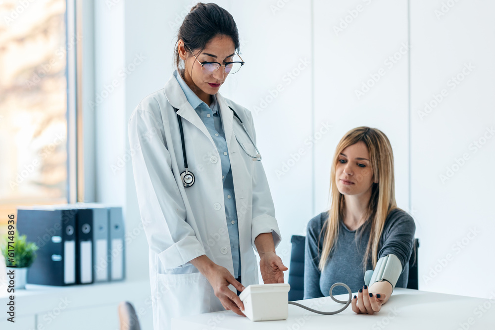 Beautiful female doctor measuring heart and blood pressure while taking care to young patient in the medical consultation Beautiful female doctor measuring heart and blood pressure while taking care to young patient in the medical consultation