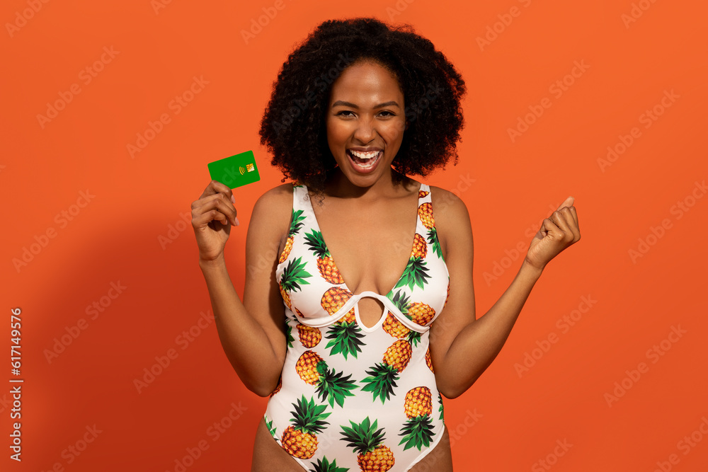 Excited black woman in swimsuit holding bank card and gesturing Excited black woman in swimsuit holding bank card and gesturing