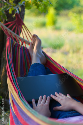 freelance. work from home with a laptop on vacation.woman with a laptop on a hammock.working in pleasure.colorful hammock.outdoor recreation.playful girl.lying on a hammock.resting in nature.relax © Daria