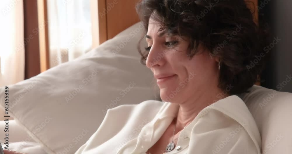 Smiling woman using digital tablet, close-up. Camera swinging softly from human hand moving on notepad to portrait of young brunette woman with curly hair, on the sofa, looking on her portable device. Smiling woman using digital tablet, close-up. Camera swinging softly from human hand moving on notepad to portrait of young brunette woman with curly hair, on the sofa, looking on her portable device.