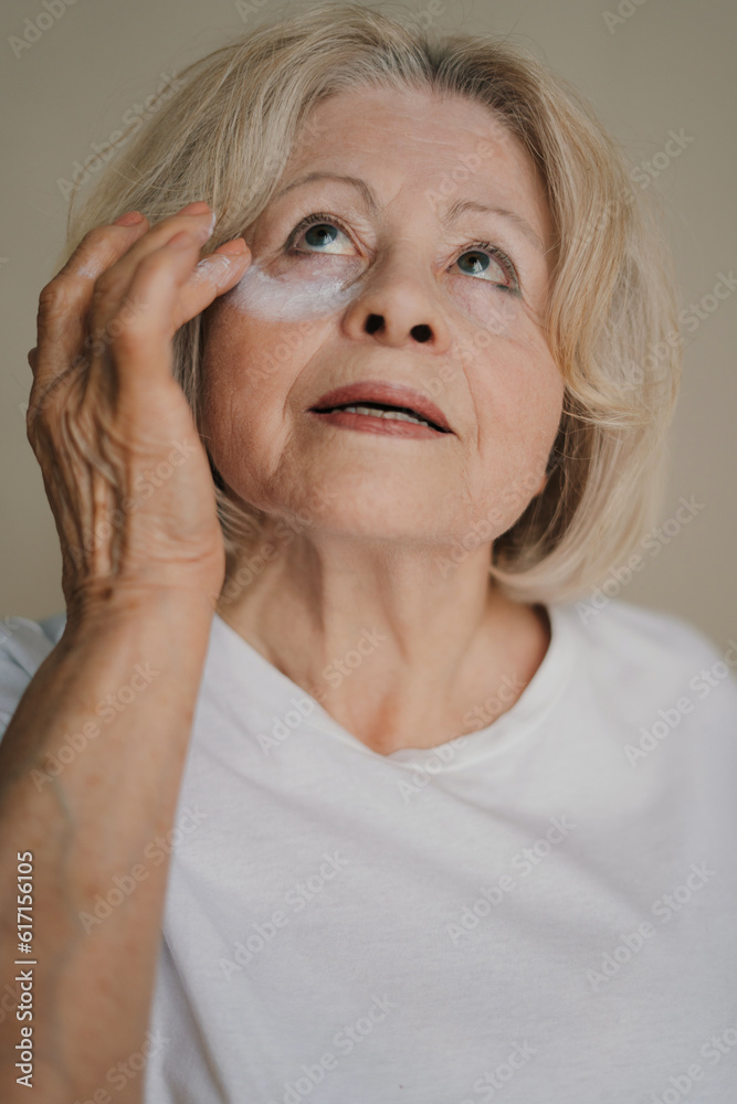 Portrait of elderly woman with gray hair looking at camera and touching face while standing against gray background Portrait of elderly woman with gray hair looking at camera and touching face while standing against gray background