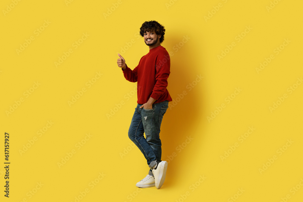 Positive handsome eastern guy showing thumb up, yellow background Positive handsome eastern guy showing thumb up, yellow background
