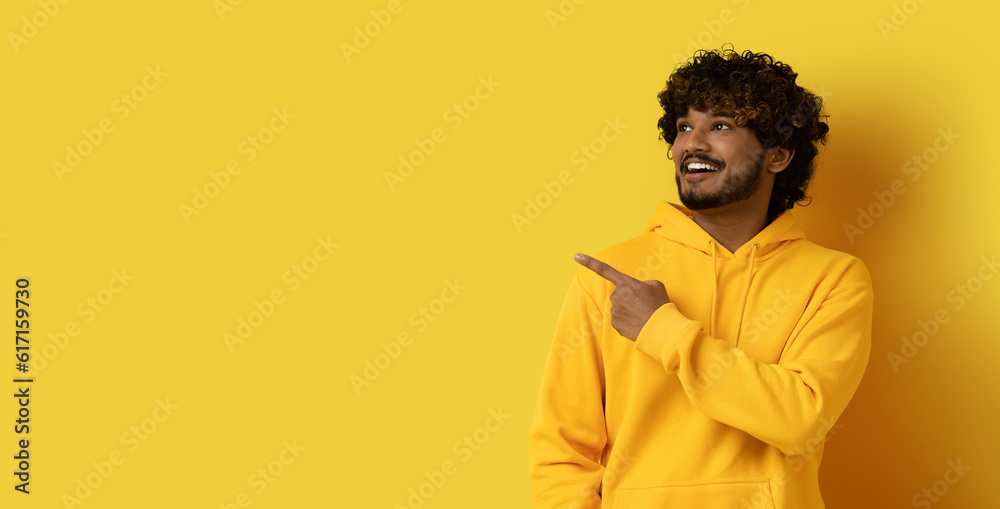 Happy millennial indian guy poitning at copy space, yellow background Happy millennial indian guy poitning at copy space, yellow background