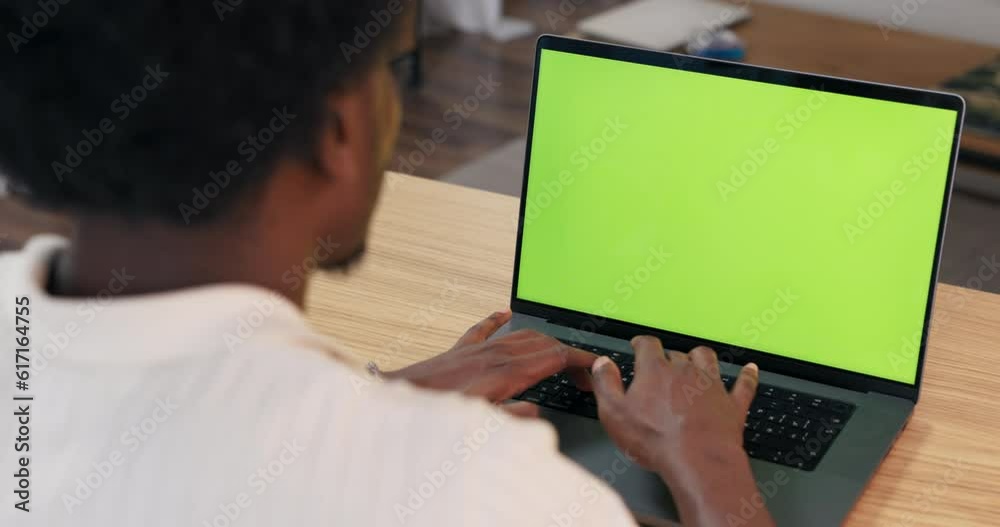 A biracial freelancer working in front of a greenscreen laptop display while sitting at a desk in a home office developing a project. A biracial freelancer working in front of a greenscreen laptop display while sitting at a desk in a home office developing a project.