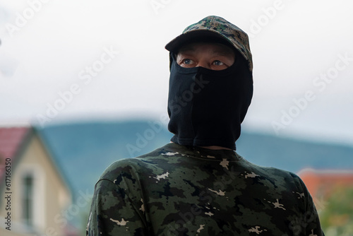 Mobilized military mercenary, balaclava hiding face, camouflage uniform, blurred background. Concept: private military company, armed conflict, war in Ukraine. photo