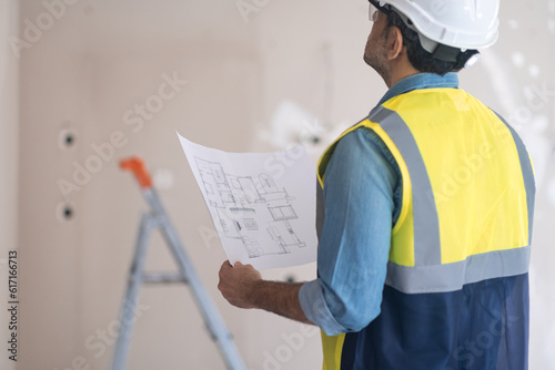 Curious engineer holding apartment drawing in hands looks at shabby wall in living room experienced man in professional uniform examining premise before renovation process