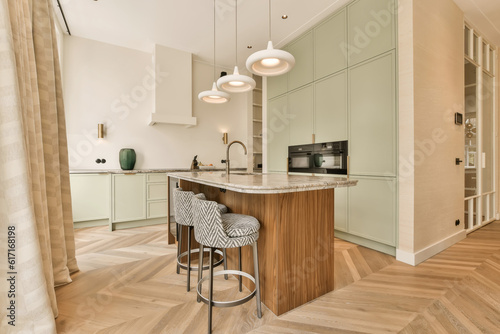 a modern kitchen with wood flooring and light green cabinets in the room is also decorated with white pendants
