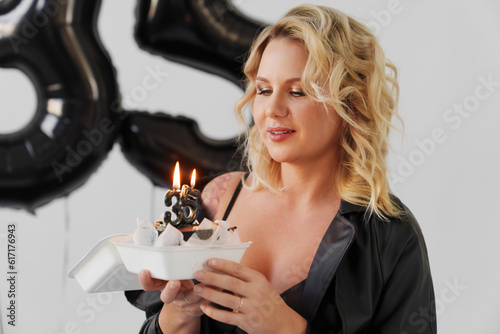 blonde woman in black with a cake with a candle number thirty-five photo