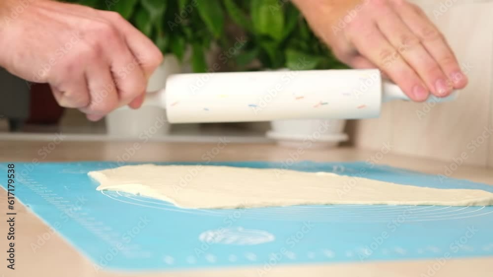 A man rolls yeast dough into a pizza layer with a silicone rolling pin on a silicone mat. Cooking homemade pizza. A man rolls yeast dough into a pizza layer with a silicone rolling pin on a silicone mat. Cooking homemade pizza.