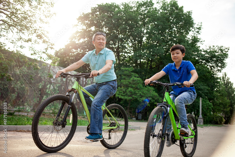 asian old father and son ride bikes together in the park, korean senior and grandpa are active with child