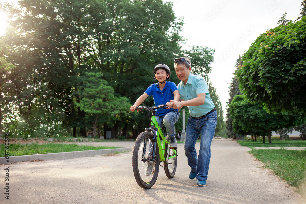 asian dad teaches son to ride bike, korean senior helps child, boy in helmet is actively relaxing with his father asian dad teaches son to ride bike, korean senior helps child, boy in helmet is actively relaxing with his father