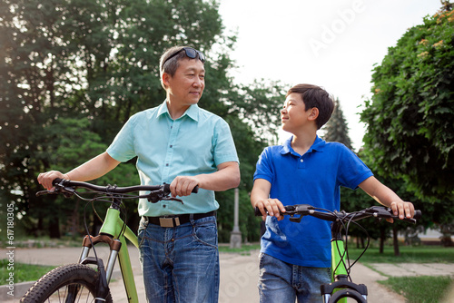asian old father and son ride bikes together in the park, korean senior and grandpa are active with child