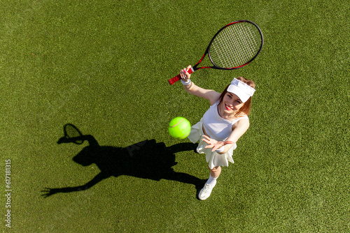 young girl tennis player in white sports uniform plays tennis on green court, woman coach with tennis racket