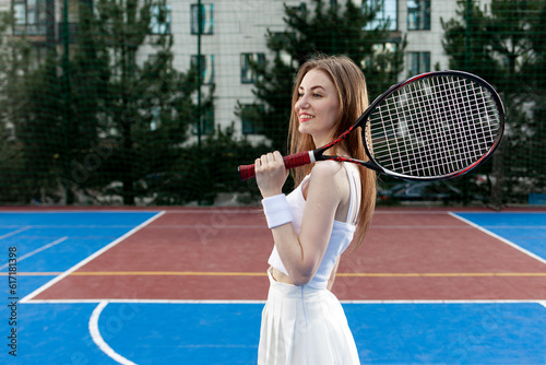 portrait of tennis player girl in white uniform with racket on blue court, female athlete stands near the tennis net © Богдан Маліцький
