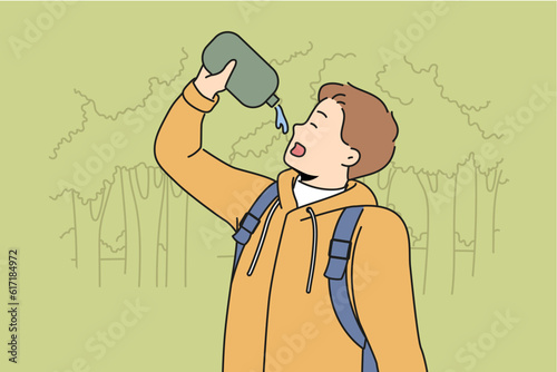 Man drinks water hiking in forest feeling thirsty after long walk through wilderness area with trees. Young guy with flask is fond of hiking and travels in national nature reserve.