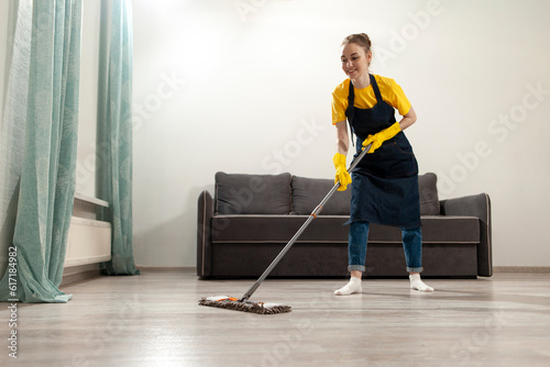 girl housewife in apron and gloves washes the floor with mop, woman cleans the room and does wet cleaning
