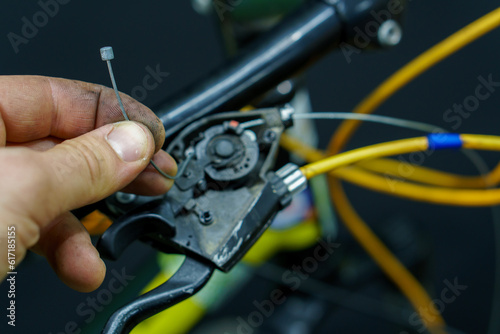 The handlebar of a mountain bike in the workshop on a black background. Replacement of the gearshift cable in the bike. The mechanic has a new cable in his hands.