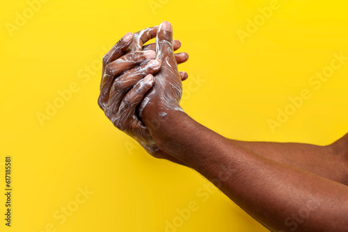 hands of African American man in soap and foam on yellow isolated background, the guy washes his hands