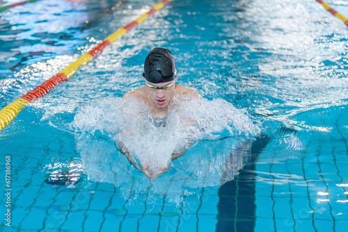 Front view of a male athlete swimming breaststroke style in the pool between two swimming lane markers. Competitive swim discipline concept.