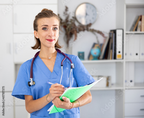 Cheefrul young woman therapist with stethoscope on shoulders holding paper folder. photo