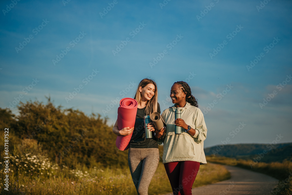 Melting Pot of Mindfulness: In a celebration of diversity and mindfulness, a black and a Caucasian woman stand tall, embodying strength and grace as they prepare to practice yoga in a natural oasis.