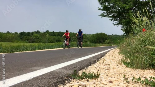 Video recorded on a sunny day from the ground. A group of three cyclists shooten from the back passing in front of the camera