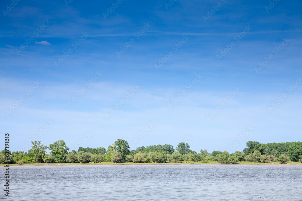 Landscape of the Danube river in Krcedin, Vojvodina, Serbia, during a sunny afternoon, facing a green forest on the riverbank. The Danube is the biggest river on Central Europe.