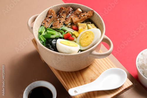 Cooking pot with tasty Chinese soup and soy sauce on color background