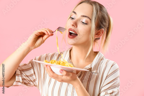 Young woman eating tasty pasta on pink background  closeup