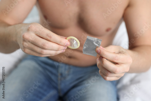 Closeup of man holding open pack and condom on bed