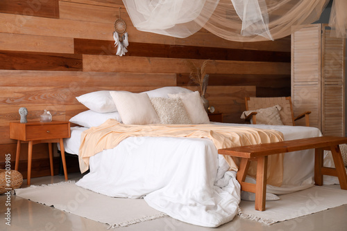 Interior of modern bedroom with bed, bench and dream catcher hanging on wooden wall